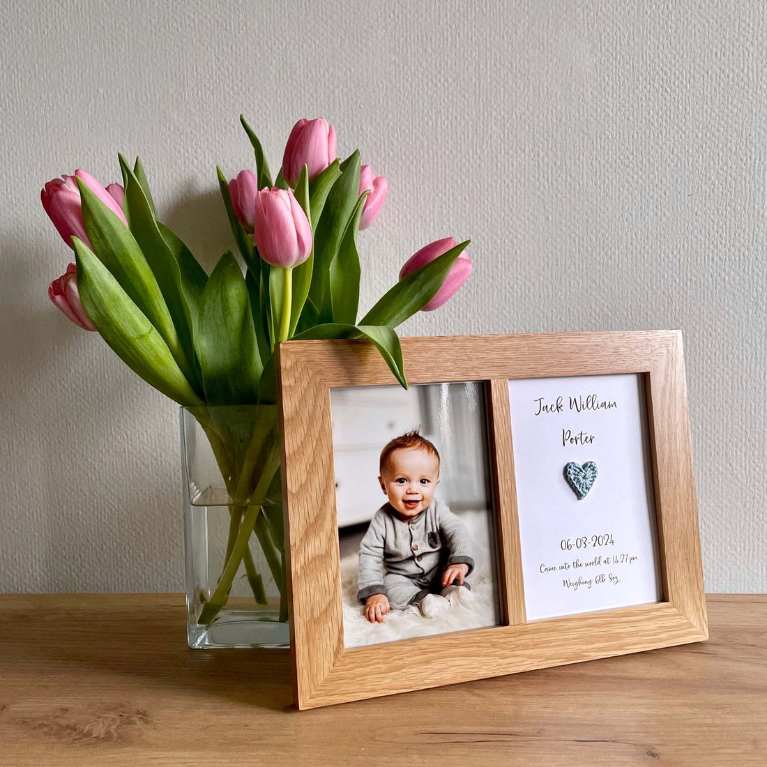 A double aperture frame displaying a Mollycat Studio personalised new baby card and baby photo. The frame is placed alongside a glass vase of pink tulips