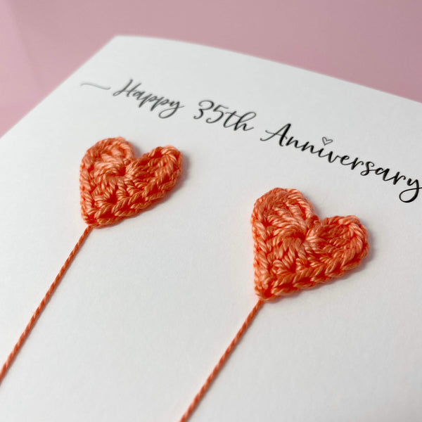 Crocheted heart shapes on a card with 'Happy 35th Anniversary' text on a pink background