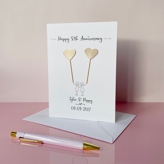 8th Anniversary card with hearts and couple illustration on a pink surface with a pen.