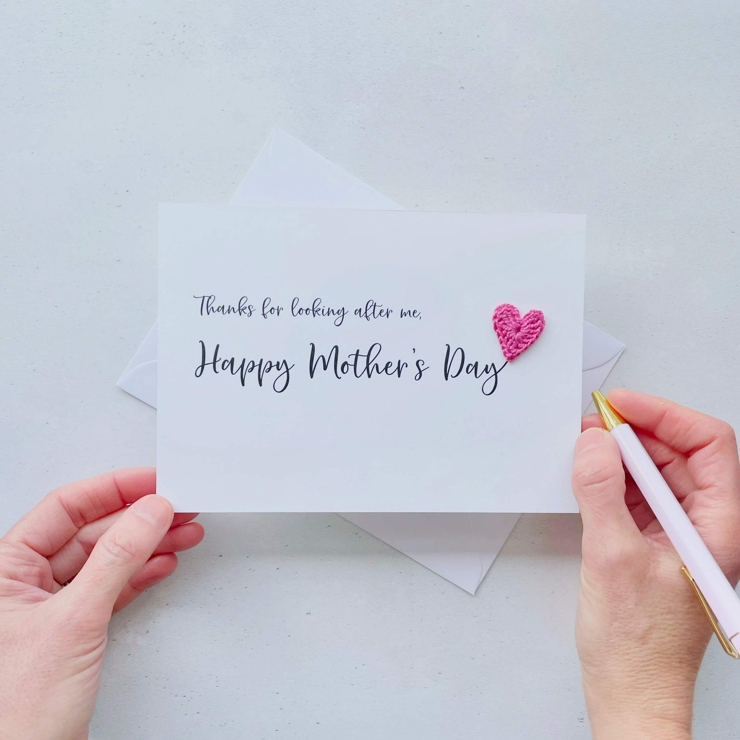 A white Mother’s Day card that has ‘Thanks for looking after me, Happy Mother’s Day’ printed on the card in black cursive text. A bright pink crochet heart has been attatched to the ‘y’ at the end. 