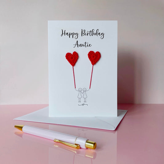 Greeting card with red crochet heart balloons and 'Happy Birthday Auntie' text. The card is on a pale pink surface. 