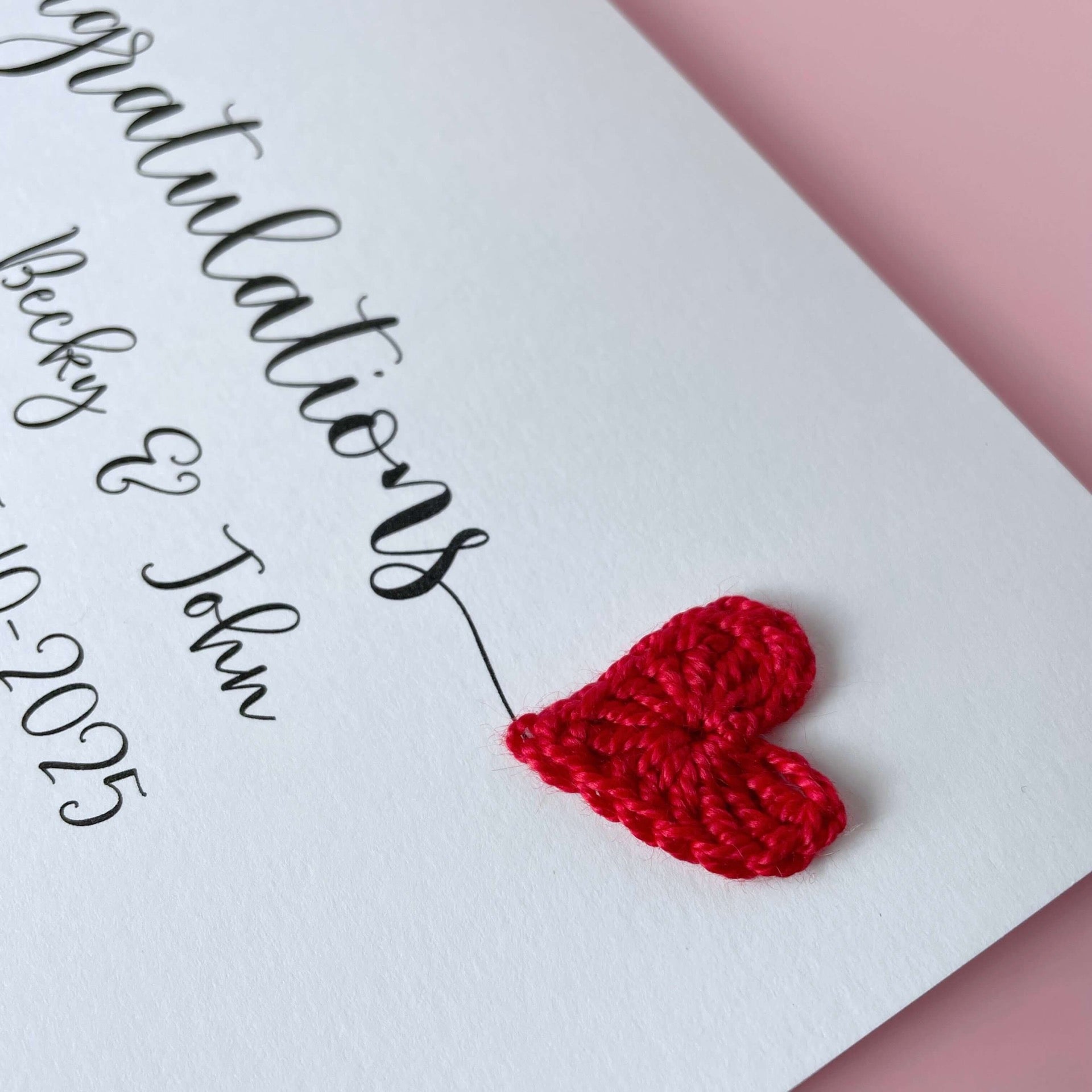 Red crochet heart on a card with 'Congratulations' text. The names of the couple are printed along with their wedding date. 
