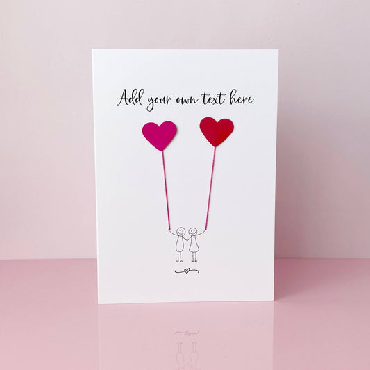 Design your own card, a simple design that features a line drawn couple each holding a pearlescent read card heart. There is space at the top of the card to add your own text.