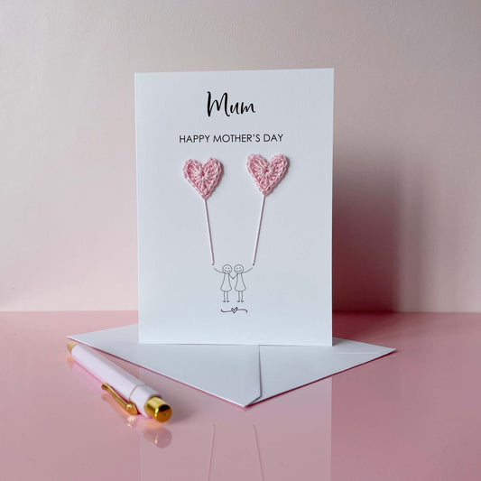 Mother's Day card with pale pink crochet heart balloons and two people on a pink background