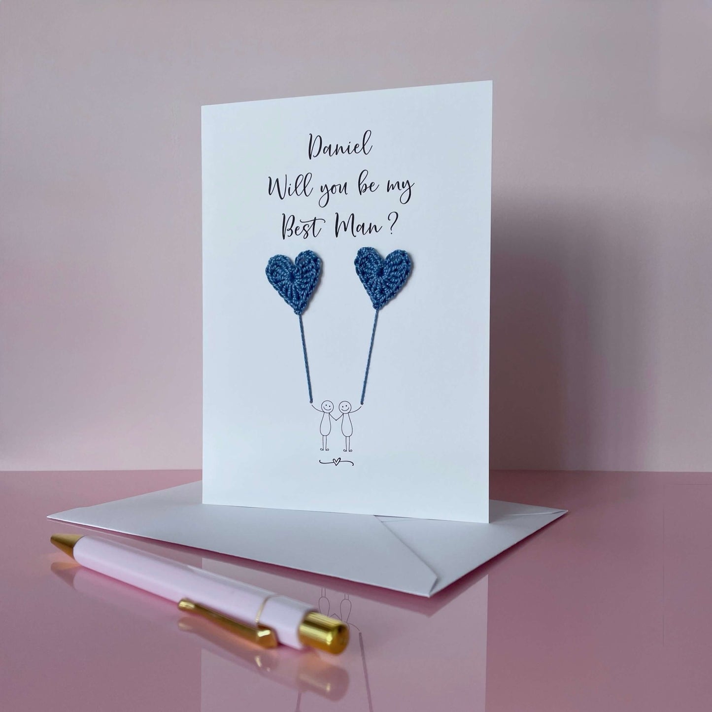 A white card with a line drawn couple printed on it - the couple are each holding a blue crochet heart balloon. Will you be my Best Man is printed at the top of the card with the option of adding a name, making it the perfect keepsake. 