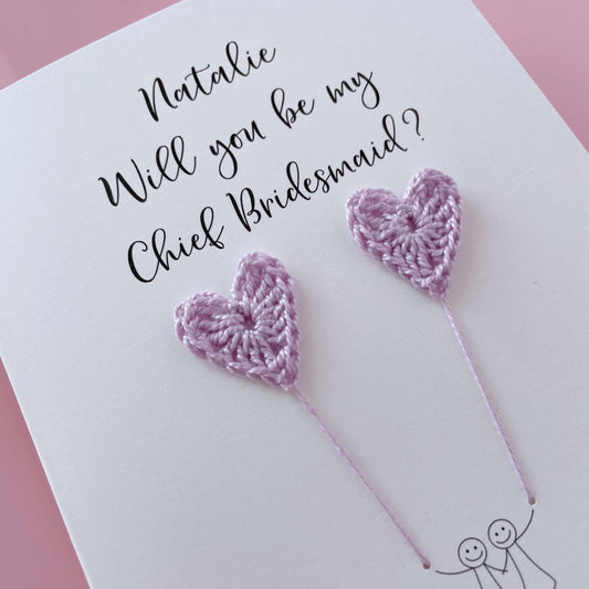 A white card with a line drawn couple printed on it - the couple are each holding a lilac crochet heart balloon. Will you be my Chief Bridesmaid is printed at the top of the card with the option of adding a name, making it the perfect keepsake. 