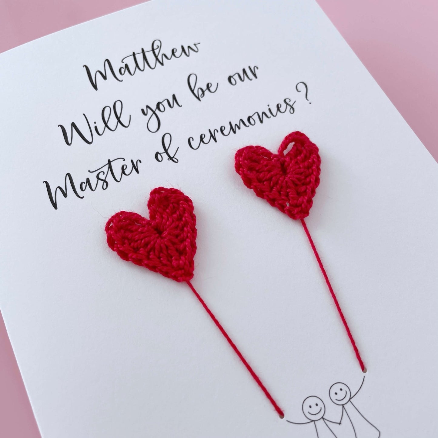 A white card with a line drawn couple printed on it - the couple are each holding a red crochet heart balloon. Will you be our Master of ceremonies is printed at the top of the card with the option of adding a name, making it the perfect keepsake. 