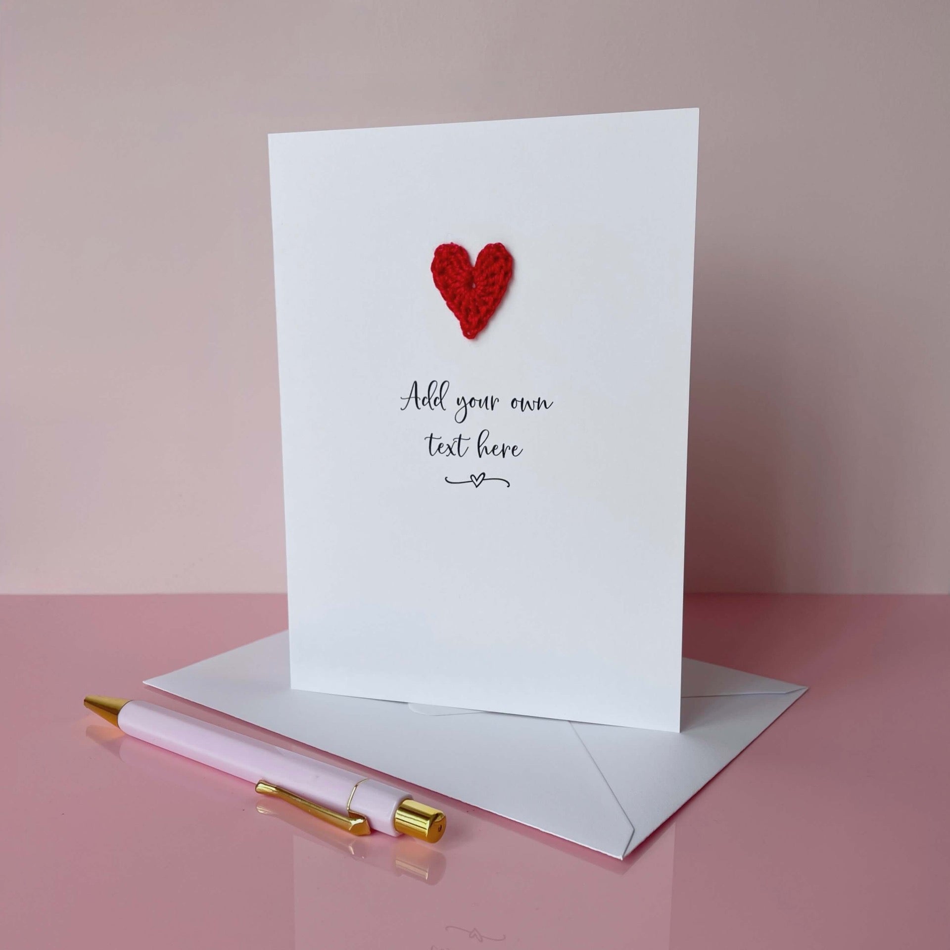 Greeting card with red heart and pen on pink surface