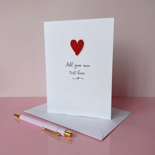 Greeting card with red heart and pen on pink surface