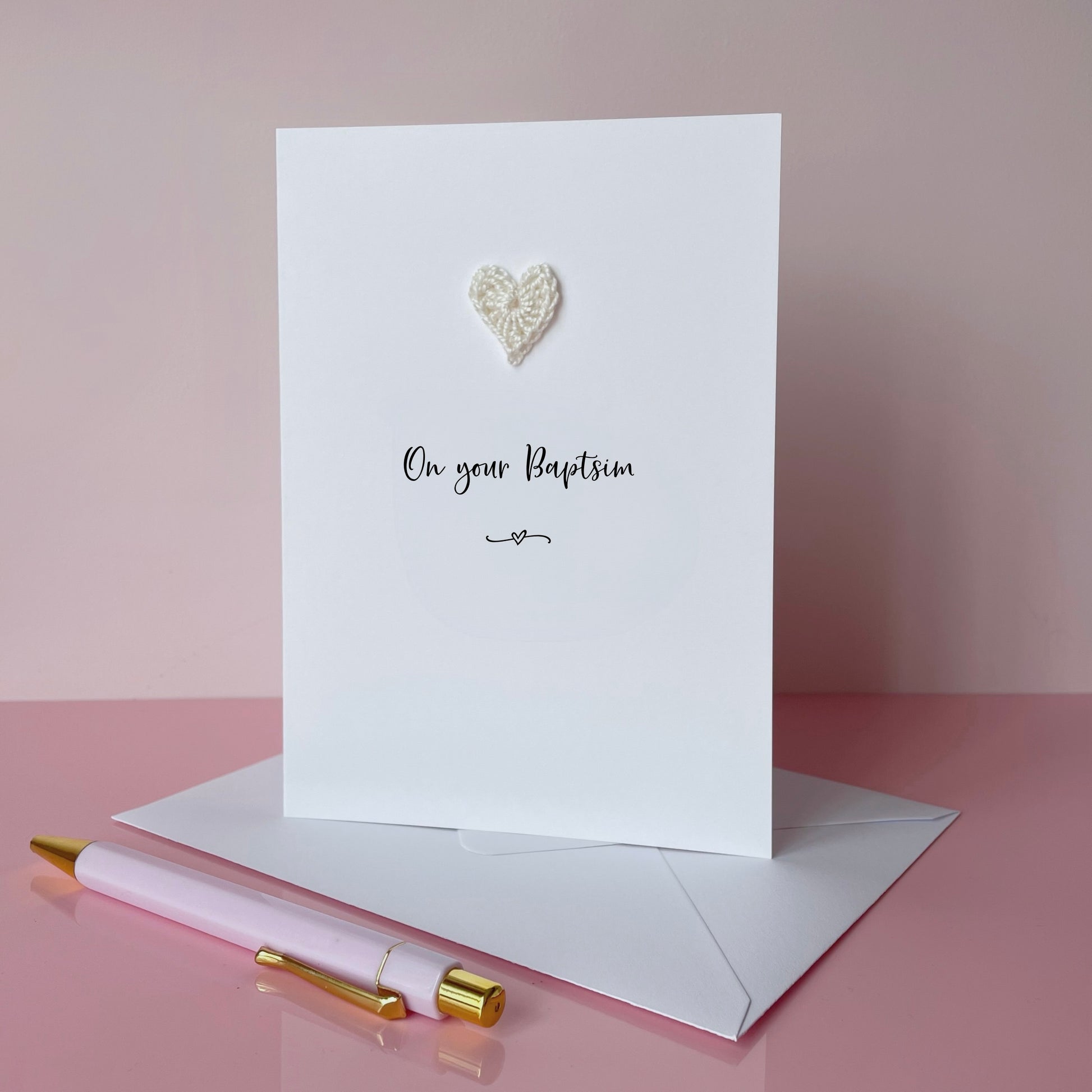 A white card with a small ivory coloured cotton crochet heart on it. On your Baptism has been printed in the centre of the card in black cursive text. 