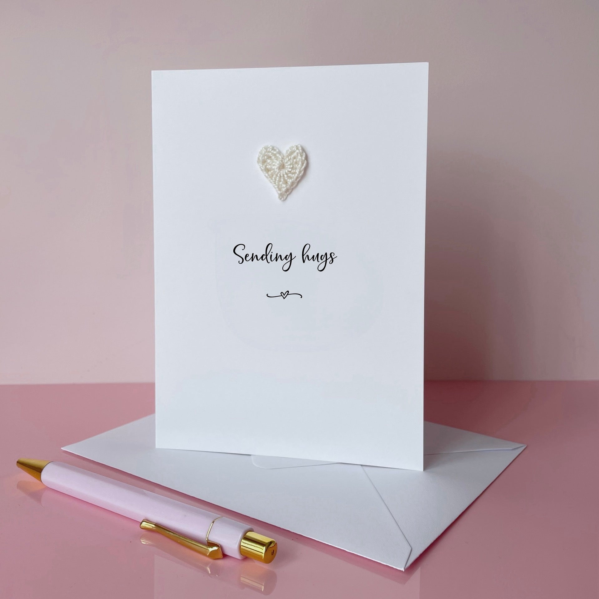 A simple card with 'Sending hugs' printed in the centre and a white crochet heart above the text. 