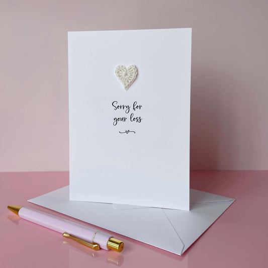 A white card with a handmade ivory coloured cotton crochet heart in the top middle. Under the heart is 'Sorry for your loss' printed in black cursive text. 