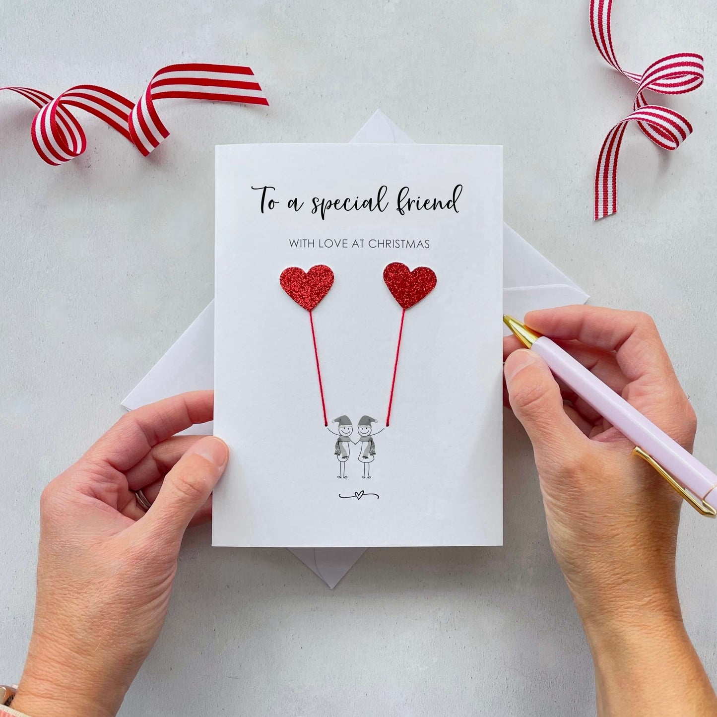 To a special friend with love at Christmas is printed at the top of the card and below the text is a line drawn couple each holding a red glitter heart balloon. 