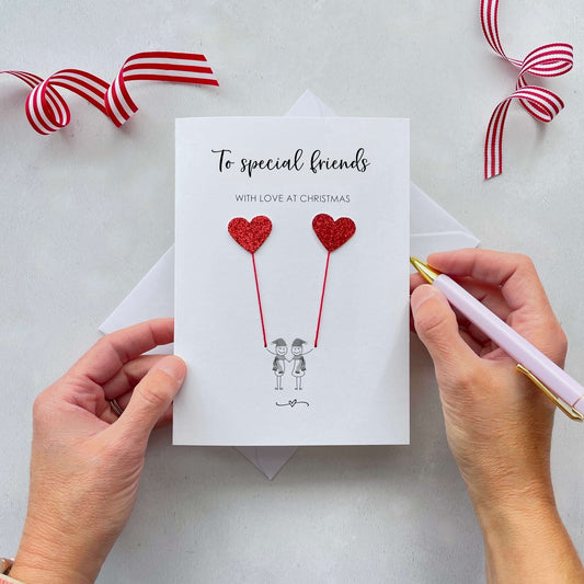 To special friends with love at Christmas is printed at the top of the card and below the text is a line drawn couple each holding a red glitter heart balloon. 