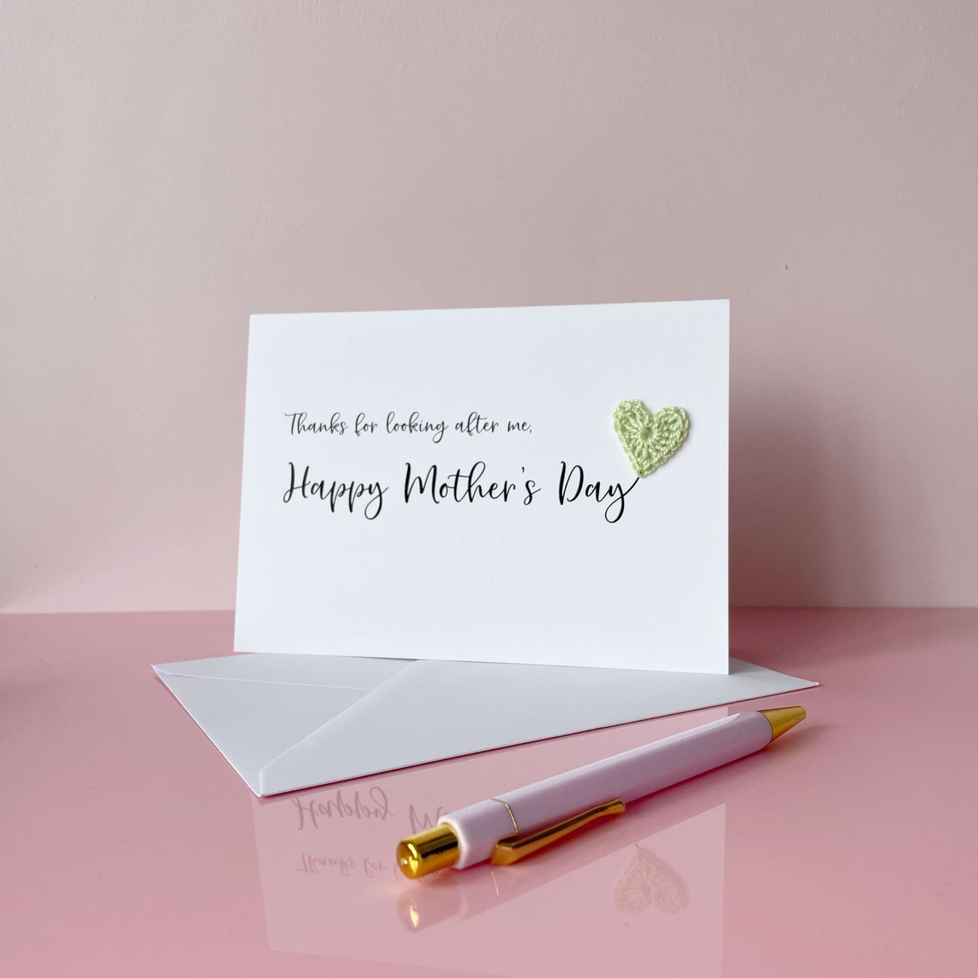 A white Mother’s Day card that has ‘Thanks for looking after me, Happy Mother’s Day’ printed on the card in black cursive text. A pale green crochet heart has been attatched to the ‘y’ at the end. 