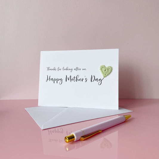 A white Mother’s Day card that has ‘Thanks for looking after me, Happy Mother’s Day’ printed on the card in black cursive text. A pale green crochet heart has been attatched to the ‘y’ at the end. 