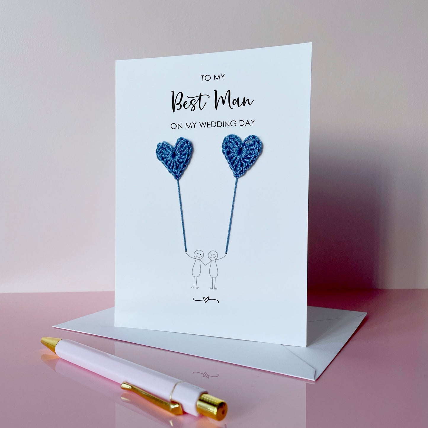 Greeting card with blue crochet heart balloons and text on a pink surface. The text at the top of the card reads 'To my Best man on my wedding day' 