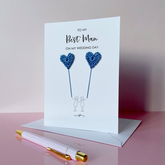 Greeting card with blue crochet heart balloons and text on a pink surface. The text at the top of the card reads 'To my Best man on my wedding day' 