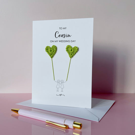 Greeting card with lime green crochet heart balloons and text on a pink surface. The text at the top of the cad reads 'To my Cousin on my wedding day' 