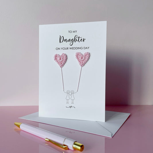 Greeting card with pink crochet heart balloons and text on a pink surface. The text at the top of the cad reads 'To my Daughter on your wedding day' 