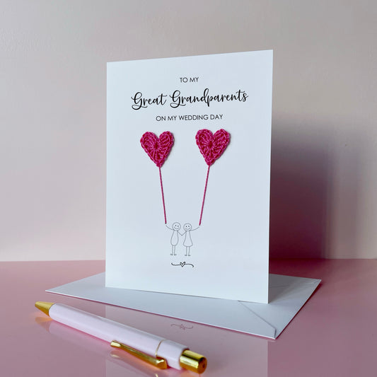 A white greeting card with bright pink crochet heart balloons and text on a pink surface. The text at the top of the cad reads 'To my Great Grandparents on my wedding day' 