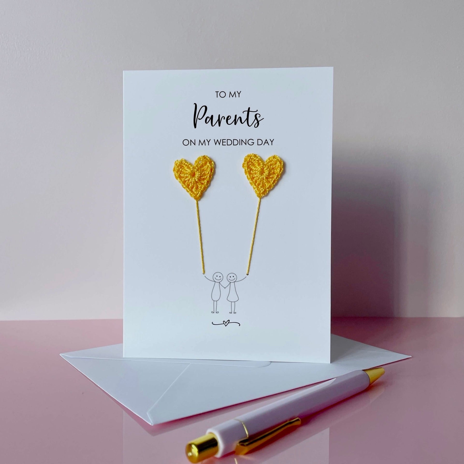 Greeting card with yellow crochet heart balloons and text on a pink surface. The text at the top of the cad reads 'To my Parents on my wedding day' 