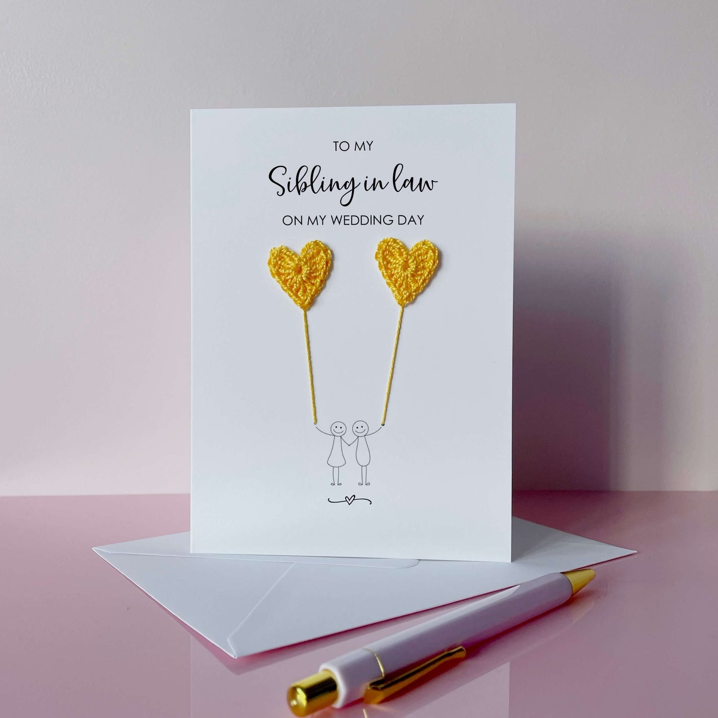 Greeting card with yellow crochet heart balloons and text on a pink surface. The text at the top of the cad reads 'To my Sibling in law on my wedding day' 