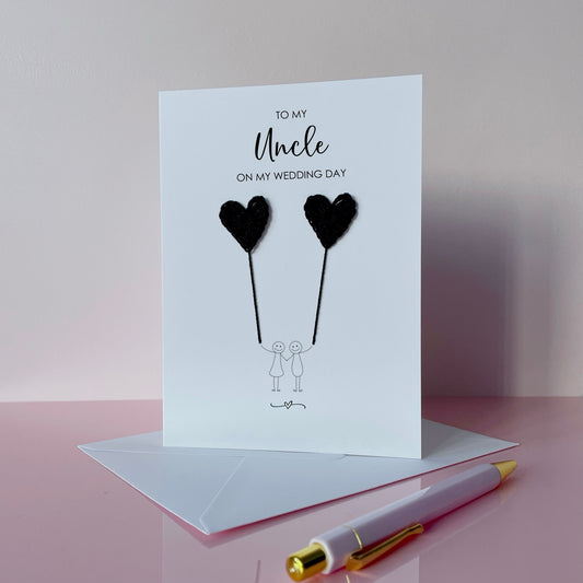Greeting card with navy blue crochet heart balloons and text on a pink surface. The text at the top of the card reads 'To my Uncle on my wedding day' 