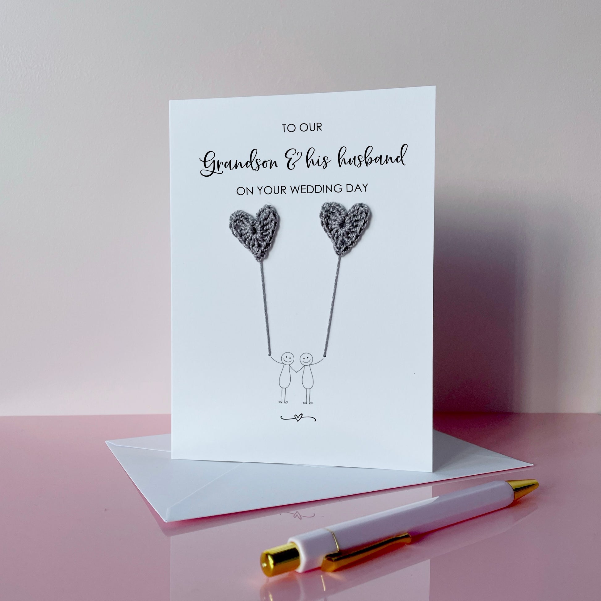 A white greeting card with grey crochet heart balloons.. The text at the top of the cad reads 'To our Grandson & his husband on your wedding day' 