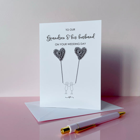 A white greeting card with grey crochet heart balloons.. The text at the top of the cad reads 'To our Grandson & his husband on your wedding day' 
