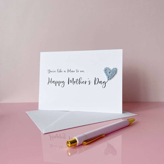 A white Mother’s Day card that has ‘You’re like a Mum to me , Happy Mother’s Day’ printed on the card in black cursive text. A pale blue crochet heart has been attatched to the ‘y’ at the end. 